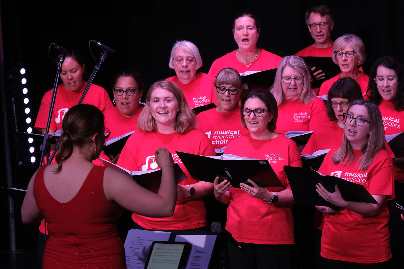 Musical Melodies Choir singing in red T-shirts, with their conductor in front of them