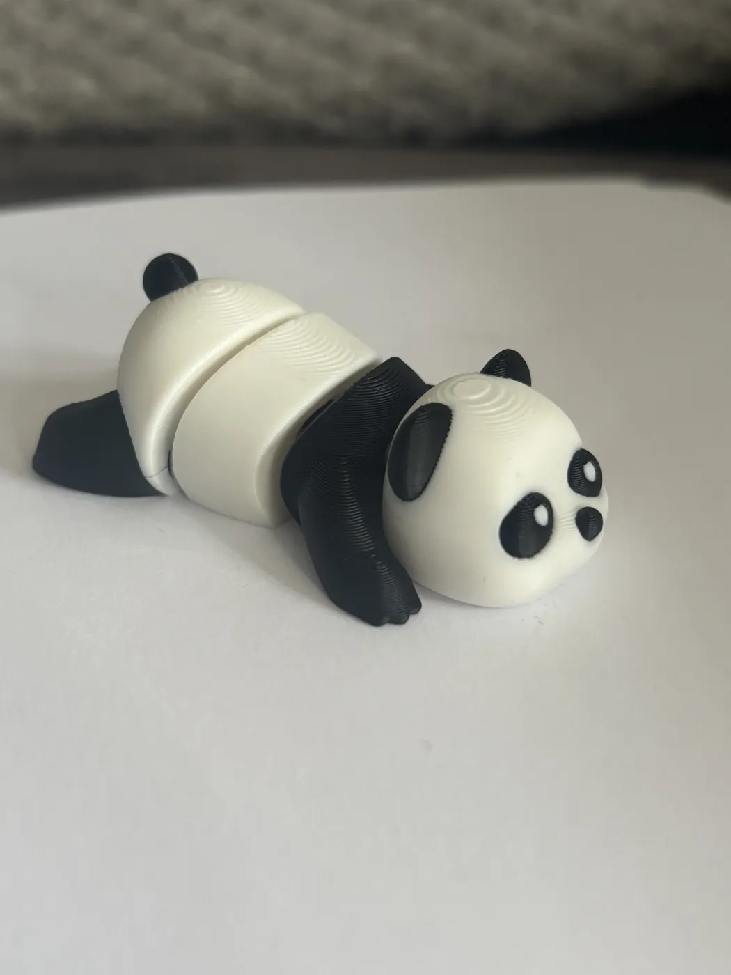 A 3D-printed panda in white and black, made in jointed sections, lying on a white surface