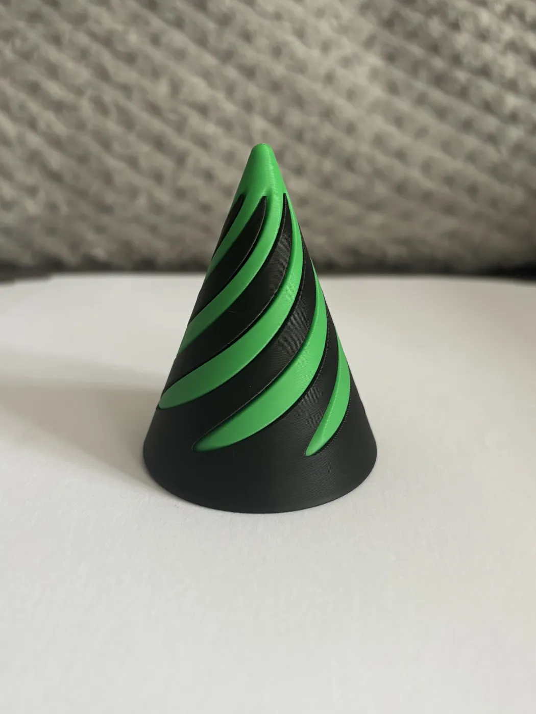 A cone-shaped 3D print with a black body and green spiral bands