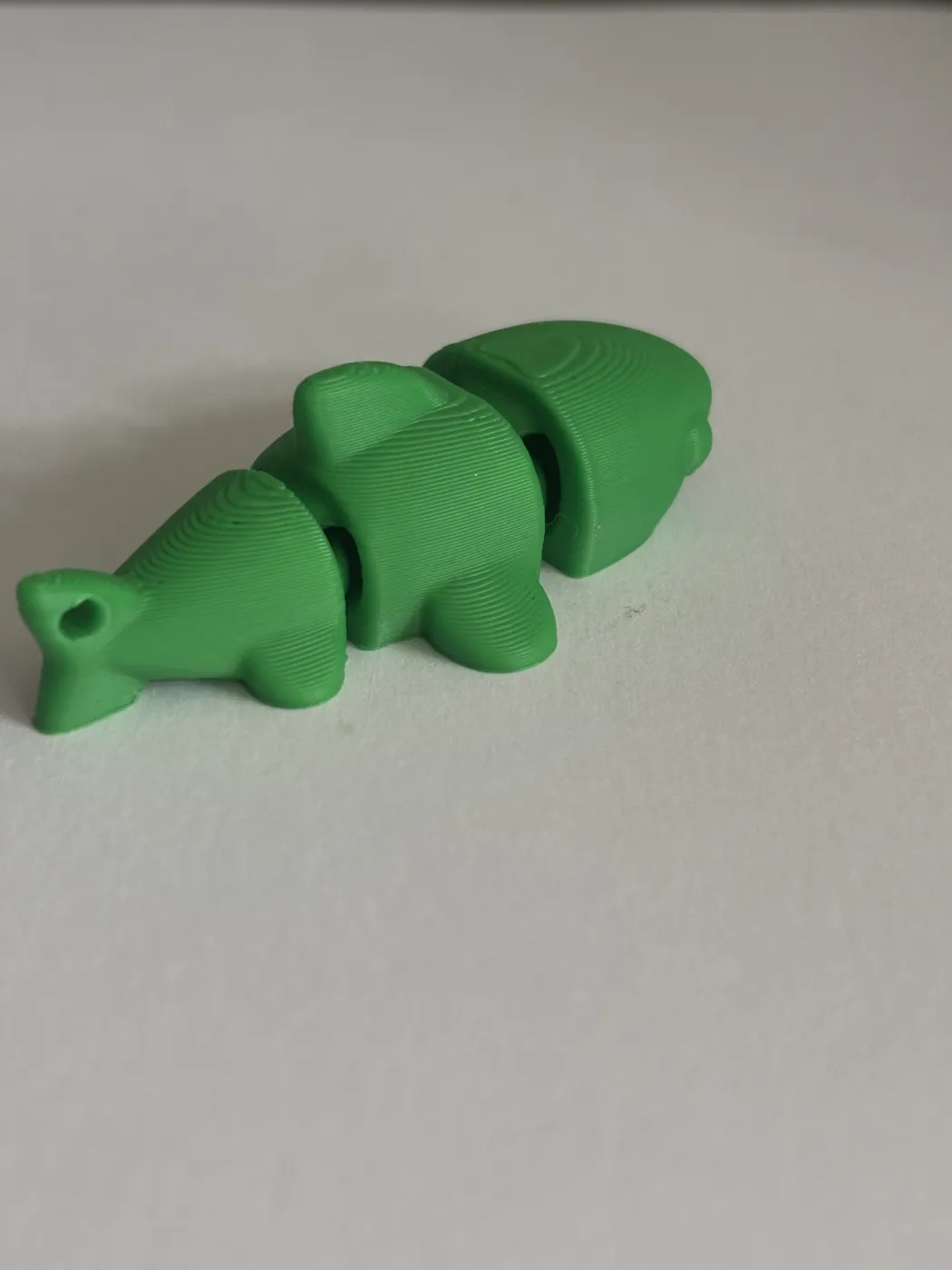 A green 3D-printed fish made in jointed sections, with a loop at the tail