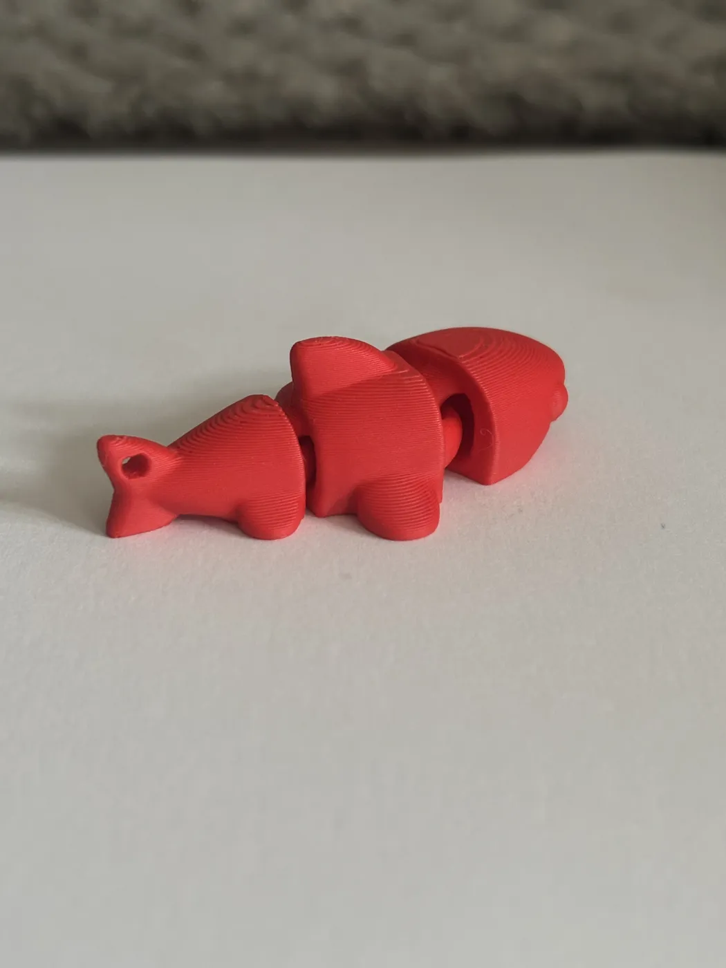 A red 3D-printed fish made in jointed sections, with a loop at the tail