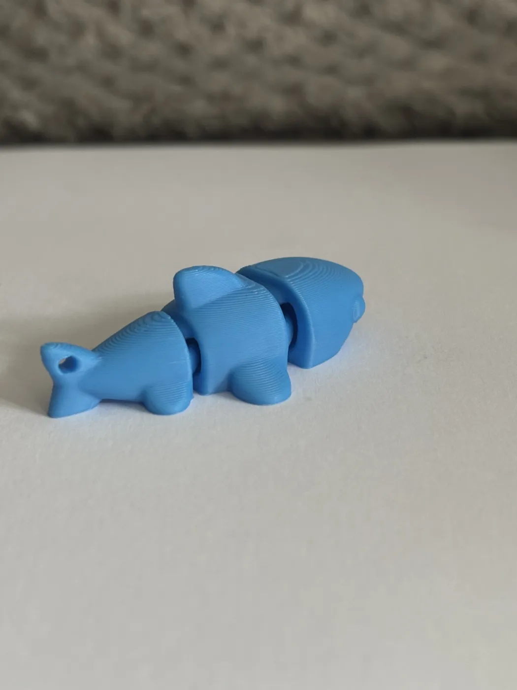 A blue 3D-printed jointed fish lying on a white surface