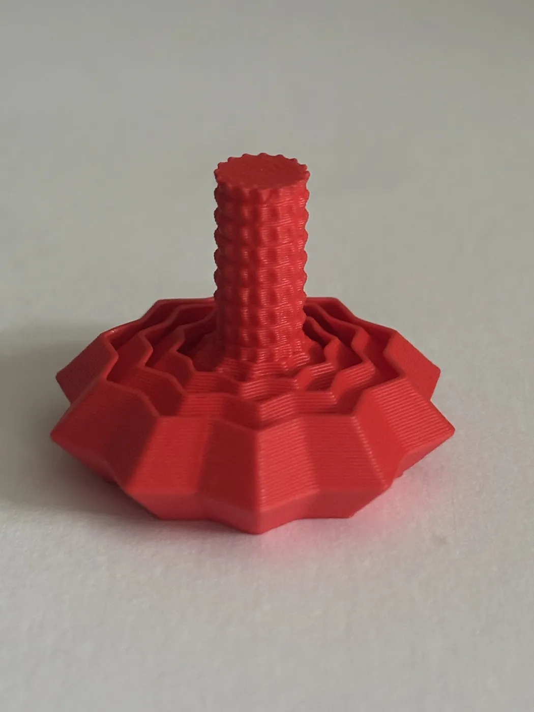 A red 3D print with a ridged, studded stem rising from a layered, many-sided base