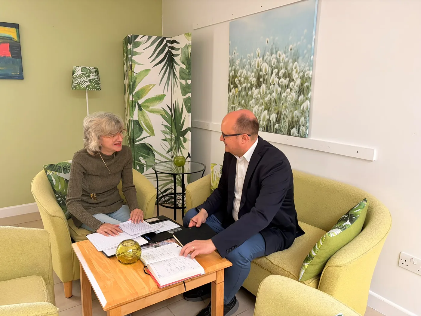 Renata Kolas and Councillor Michał Siewniak talking across a low table covered in notes and an open diary, in green armchairs at the Focolare Centre for Unity