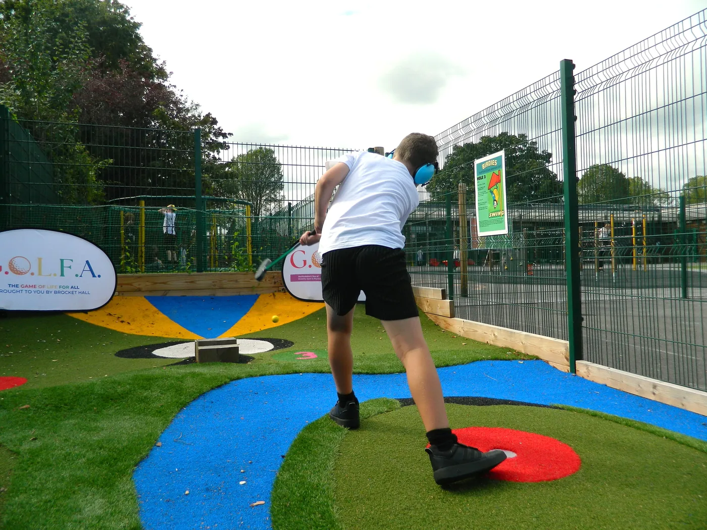 A pupil in a white T-shirt swinging a putter on a brightly coloured adventure golf hole in a school playground