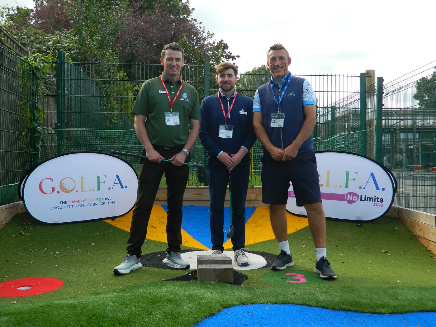 Three men wearing visitor lanyards standing on the adventure golf course between two GOLFA banners